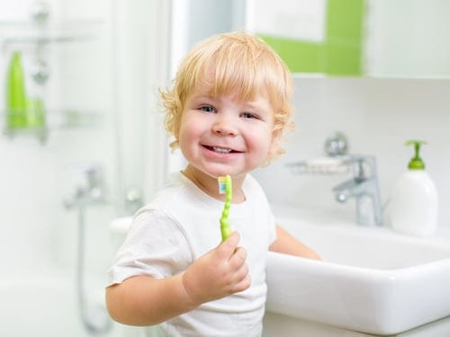 happy 5-year old boy holding his green toothbrush by the sink