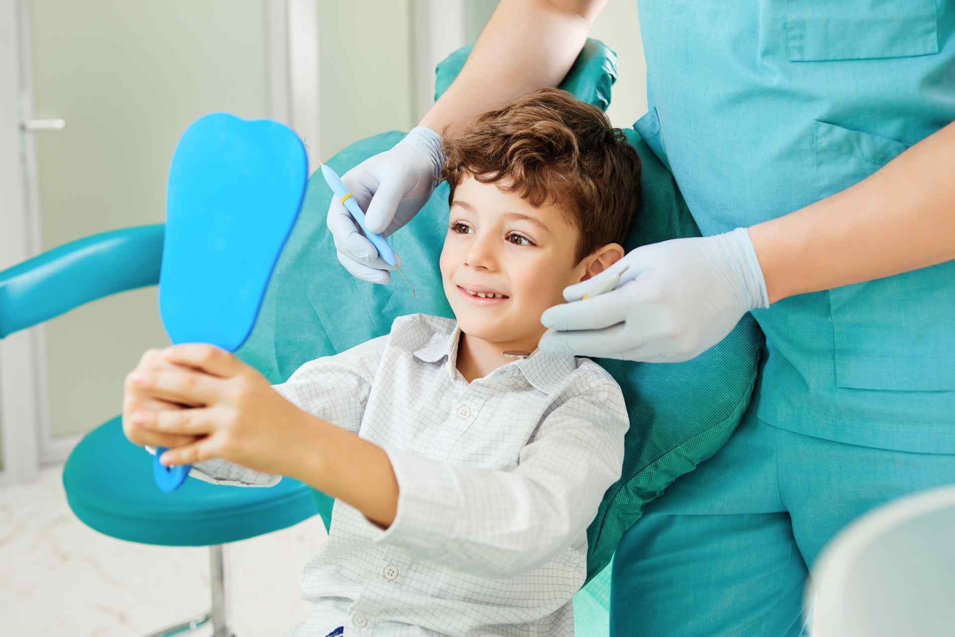 young boy at the dentist holding a hand mirror and smiling