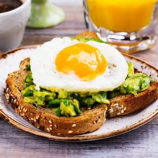 Plate of eggs and avocado toast topped with fresh seasoning, served on whole-grain bread for a healthy, balanced meal.