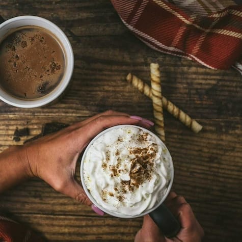 Overhead view of a festive holiday drink topped with swirls of whipped cream, sprinkled with seasonal spices, and served in a cozy, winter-themed setting